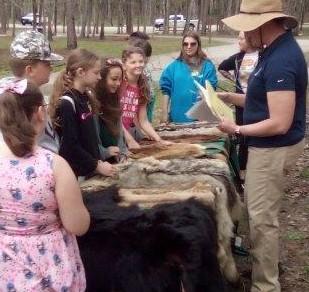 Students and presenter gathered around table with furs at the mammal fur station at the Eco Day at the Piney Wood Rec Area